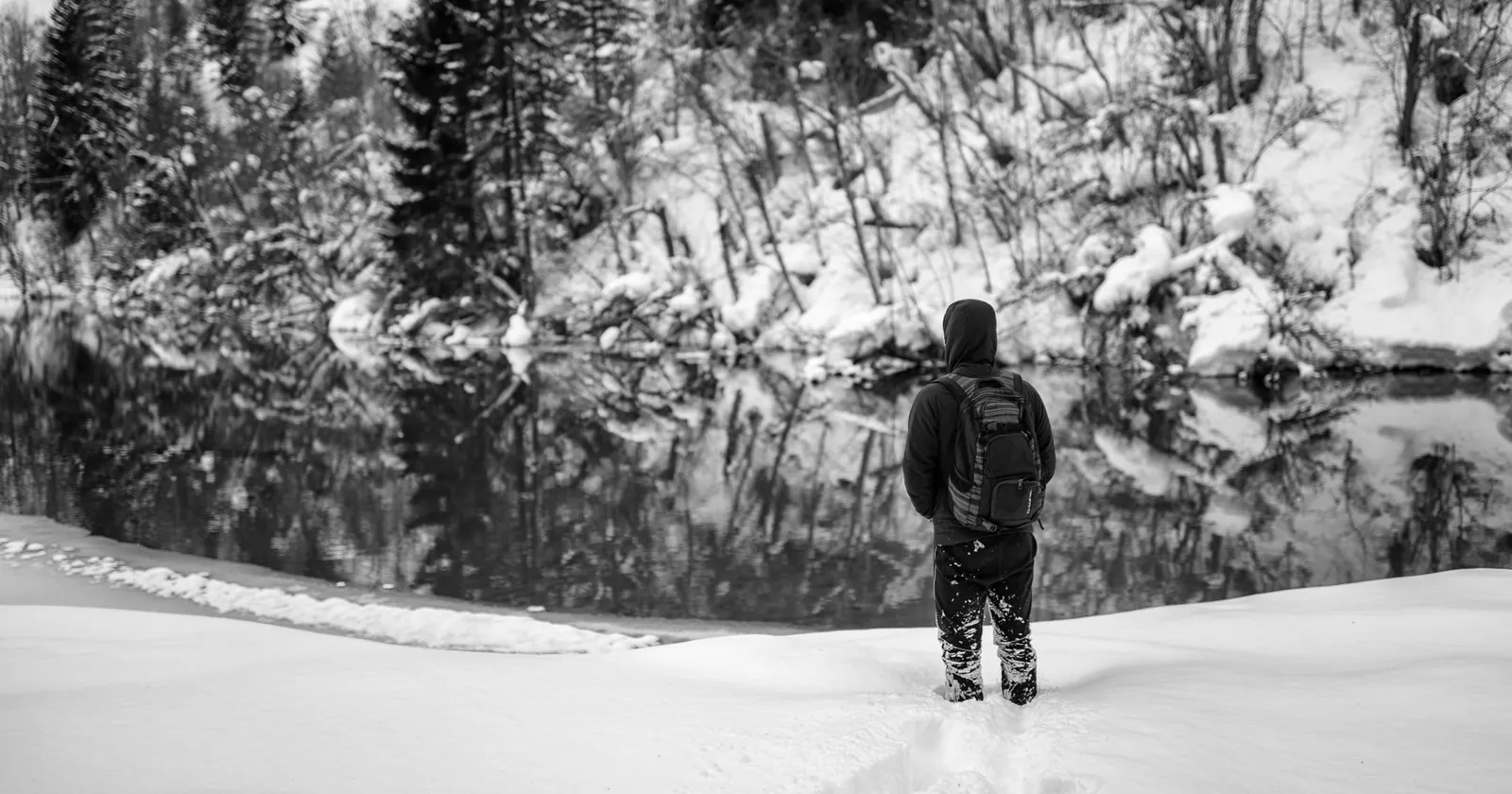 Cla Mosca von hinten im Tiefschnee, vor ihm ein stiller Bergsee, schwarzweiss